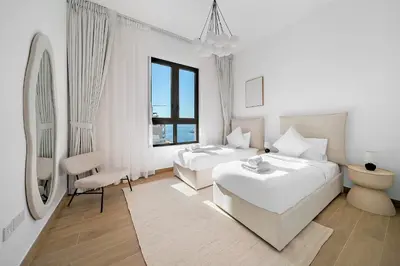 a white bedroom with two beds and a mirror at VayK - Modern 2BR with Stunning Sea View in Port de La Mer in Dubai