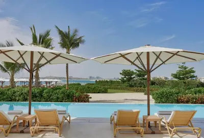 a group of chairs and umbrellas next to a swimming pool at Highend Seven Palm 1BR Private Beach and Infinity Pool in Dubai