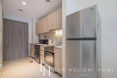 a kitchen with a stainless steel refrigerator and wooden cabinets at LUX Dubai Hills Sway Studio 2 in Dubai