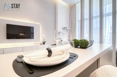 a white kitchen with a table with glasses and a tv at Luxurious Spacious Studio in Dubai