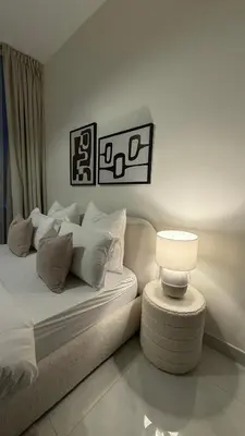 a white bedroom with a bed and a table with a lamp at Appartement de Luxe 1 Chambre avec Piscine Privée sur Balcon in Dubai