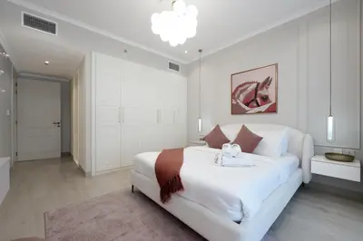 a white bedroom with a large bed and a chandelier at Stylish JVC 2BR Stay with Guest Room Rose Gold Accents in Dubai