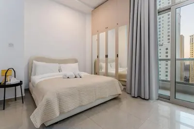 a white bedroom with a bed and a large window at Marina Wharf 1 Bedroom with JBR Beach Views in Dubai