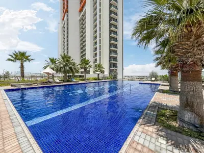 a pool with palm trees and a tall building at Contemporary 1BR Home in Damac Hills in Dubai