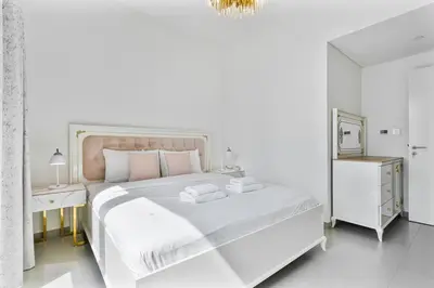 a white bedroom with a large white bed with pink pillows at 3BR APT with Burj View from Balcony - Pool and Gym in Dubai