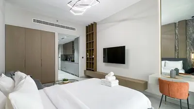 a white bedroom with a large bed and a tv at Modern Studio in JVC, Rooftop Pool & Gym Access - 10AB08 in Dubai