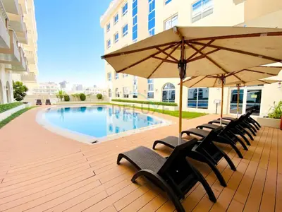 a deck with chairs and an umbrella next to a pool at Studio with Balcony Overlooking the Community, Walking Distance from the Park, Hanover Square HSS, Jumeirah Village Circle by Deluxe Holiday Homes in Dubai