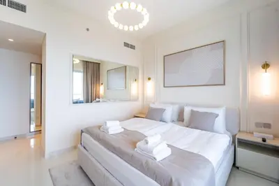 a white bedroom with a large bed and a mirror at Elie Saab Tower Luxury Apartment in Dubai