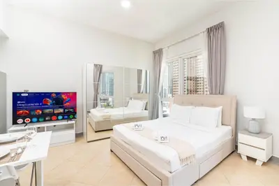 a white bedroom with a large bed and a tv at PVH - Sunny Studio near Metro - Madison Residency in Dubai