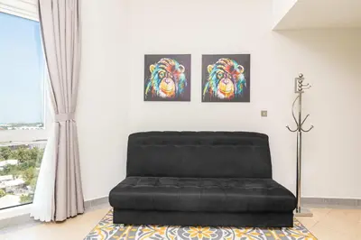 a black leather couch in a living room with paintings on the wall at PVH - Sunny Studio near Metro - Madison Residency in Dubai