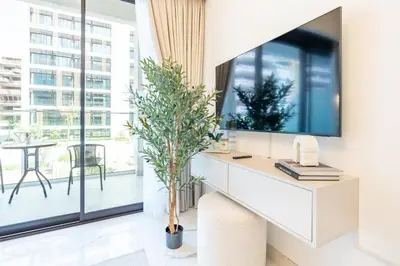 a living room with a tv and a desk with a plant at Pool and Community View Studio, Near Top Landmarks, Azizi Riviera 59, Al Merkadh by Deluxe Holiday Homes in Dubai