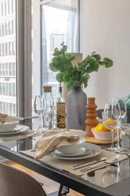 a dining table with plates and a vase with a plant at Lavish 2BR - Study with Spacious Balcony in DIFC in Dubai