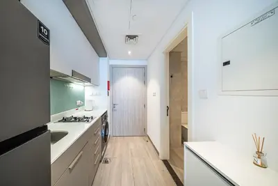 a kitchen with white counters and a hallway with a door at Studio in Dubai Production City in Dubai