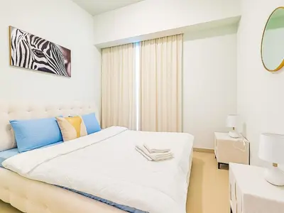 a white bedroom with a white bed with blue accents at Dream Shoma Upscale 3BR in Downtown Dubai in Dubai