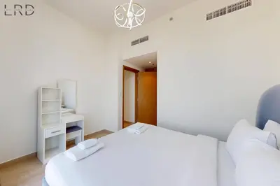 a white bedroom with a bed and a desk at Charming 1BR with Canal View in Dubai