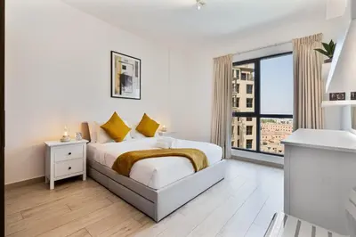 a white bedroom with a bed and a large window at Serene 1BR Stay with Pool, Gym, & Kids Playground in Dubai