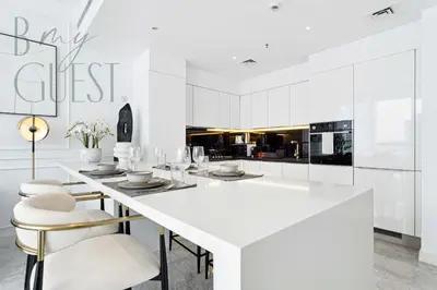 a white kitchen with a large white island with stools at Remarkable one BR in Business Bay with Canal View in Dubai