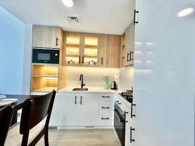 a kitchen with white cabinets and a table and a sink at Homes2Retreat - Modern Comforts 1 BR in Liva Lush Living in Dubai