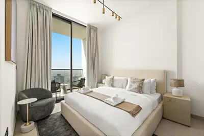a white bedroom with a large bed and a chair at VayK - Stylish Bright 1BR in JVC in Dubai