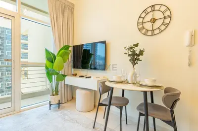 a living room with a table and a clock on the wall at Studio with Balcony Facing the Community, Located Near Golf Clubs and Cricket Stadium, Royale Residence 1 , Dubai Sports City by Deluxe Holiday Homes in Dubai