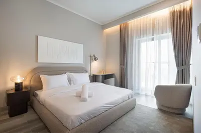 a white bedroom with a bed and a chair at Luxury 1 BHK in Jumeirah Village Circle BydPie Concept 302 in Dubai
