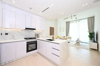 a white kitchen with white cabinets and a living room at Golden Stays - Binghatti Amber I Luxury 1BR Apartment I Fully Furnished I Pool & Gym in Dubai