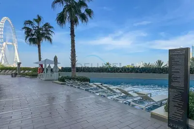 a swimming pool with lounge chairs and a ferris wheel at 3BR Overlooking Sea, Ain Dubai, and Bluewaters Island, Walking Distance to the Beach, The Address Residences, Jumeirah Beach Residence by Deluxe Holiday Homes in Dubai