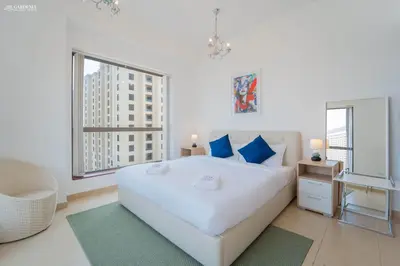 a white bedroom with a large white bed and two windows at Gardenia Bahar Suites 1 Bedroom Apartment in JBR with 2 mins walk to the Beach in Dubai