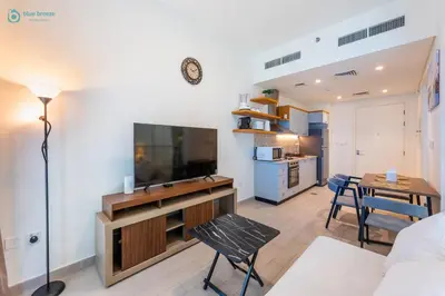 a living room with a television and a table and chairs at Blue Breeze - Modern 1BR, Dubai Hills, in Dubai