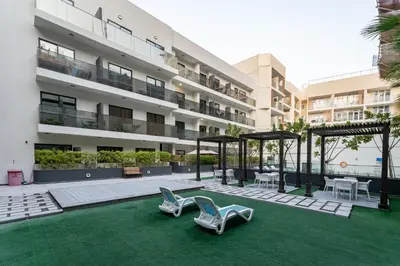 a building with two chairs on a green lawn at Lux & New 2 BHK in Jumeirah Village Circle I Close to everything I Pool I High Speed Internet I Balcony in Dubai