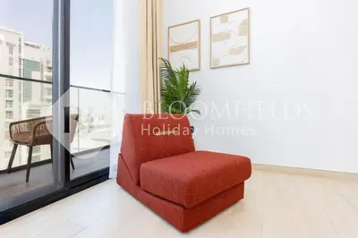 a red chair in a room with a window at Bloomfields Cozy 1BR Binghatti Nova in Dubai