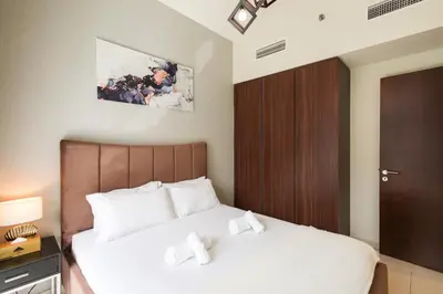 a bedroom with a bed with white sheets and a wooden door at Comfy 1BR with Large Balcony - 15-min to Mall & Burj in Dubai