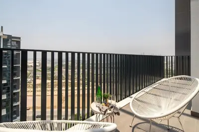 a balcony with two chairs and a table and a fence at Frank Porter - Kensington Waters, Sobha Hartland in Dubai