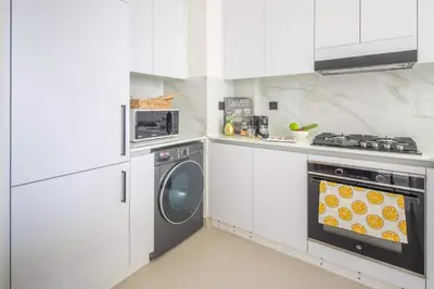 a kitchen with white cabinets and a washer and dryer at Frank Porter - Binghatti Amber in Dubai