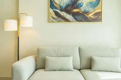 a white couch with two pillows sitting under a painting at Stylish Comfort Modern 1BR Apt Prime Location JVC in Dubai