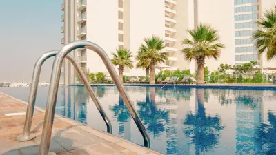 a swimming pool with palm trees and buildings at KeyRock Golf Gate - Relax and Unwind with Pool and Sauna in Dubai