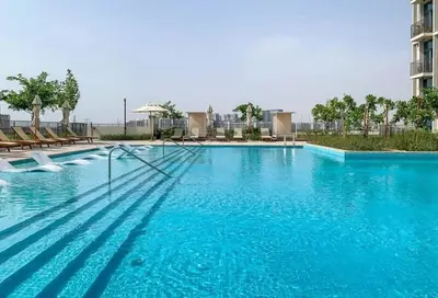 a large blue swimming pool with chairs and a building at New Luxury 1 Bed - Opposite Dubai Hills Mall in Dubai