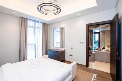 a white bedroom with a bed and a living room at Luxe 1BR Suite Dubai Dream Stay with Pool and Gym in Dubai