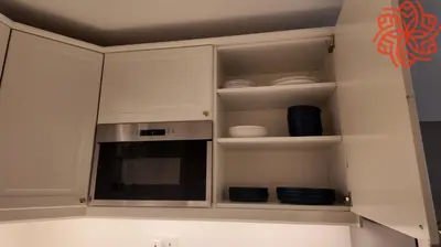 a kitchen with white cabinets with plates and a microwave at Amazing 3 bedrooms in Mayas geneva in Dubai