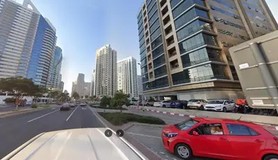 a red car driving down a city street with tall buildings at Small Partition Room Barsha Heights Tecom in Dubai