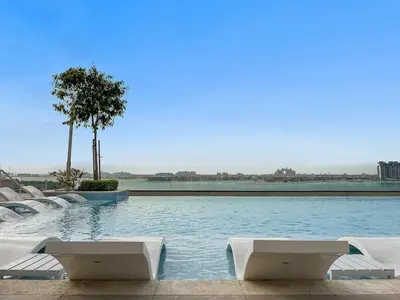 a swimming pool with white lounge chairs and a tree at FIRST CLASS 2BR Sea & Palm View, Beachfront in Dubai