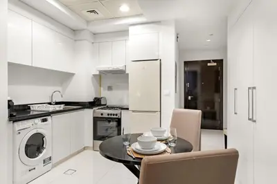 a white kitchen with a table and a dishwasher at Modern JVC Studio with Pool Gym and Easy Access to Attractions in Dubai