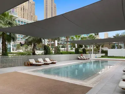 a swimming pool with chairs and a large umbrella at Stylish 1BR Apartment in JBR with Beach Access & Dubai Marina Views in Dubai