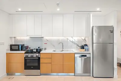 a kitchen with white cabinets and a stainless steel refrigerator at Stylish 1BR Apartment in JBR with Beach Access & Dubai Marina Views in Dubai