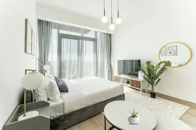 a white bedroom with a bed and a large window at HAVN - High Floor Studio in Bloom Towers, JVC in Dubai