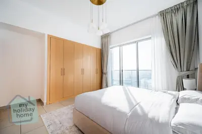 a bedroom with a white bed and a large window at Beautiful 1BR-Fully Furnished- Balcony-Pool & Gym in Dubai