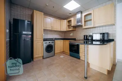a kitchen with wooden cabinets and a black refrigerator at Beautiful 1BR-Fully Furnished- Balcony-Pool & Gym in Dubai