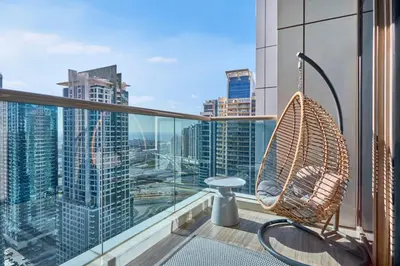 a rattan chair on a balcony with a view of a city at Sky-High Luxury 1BR in 27th Floor MBL Residence in Dubai