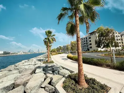 two palm trees on a sidewalk next to the water at Stylish Apartment - Private Beach - Port de La Mer in Dubai