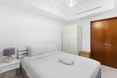 a bedroom with a white bed and a wooden cabinet at Sleek and Spacious 2BR at Dubai Marina, Near Beach in Dubai